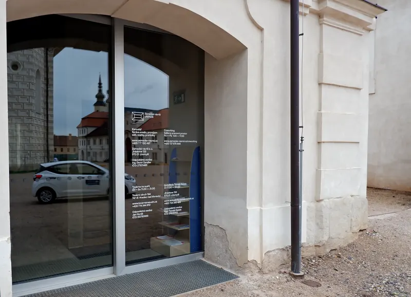 Prosklený vchod do Kočárovny v&nbsp;oblouku, ve skle se odráží zámek
